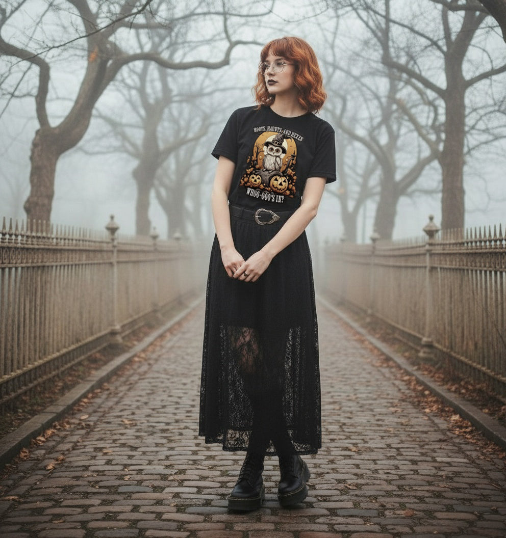 Person wearing a black t-shirt with a graphic design and a long black dress standing on a foggy path.