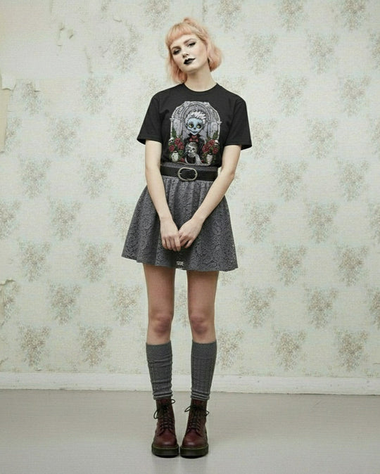 Person wearing a black t-shirt with a graphic design, gray skirt, and knee-high socks against a floral wallpaper background.