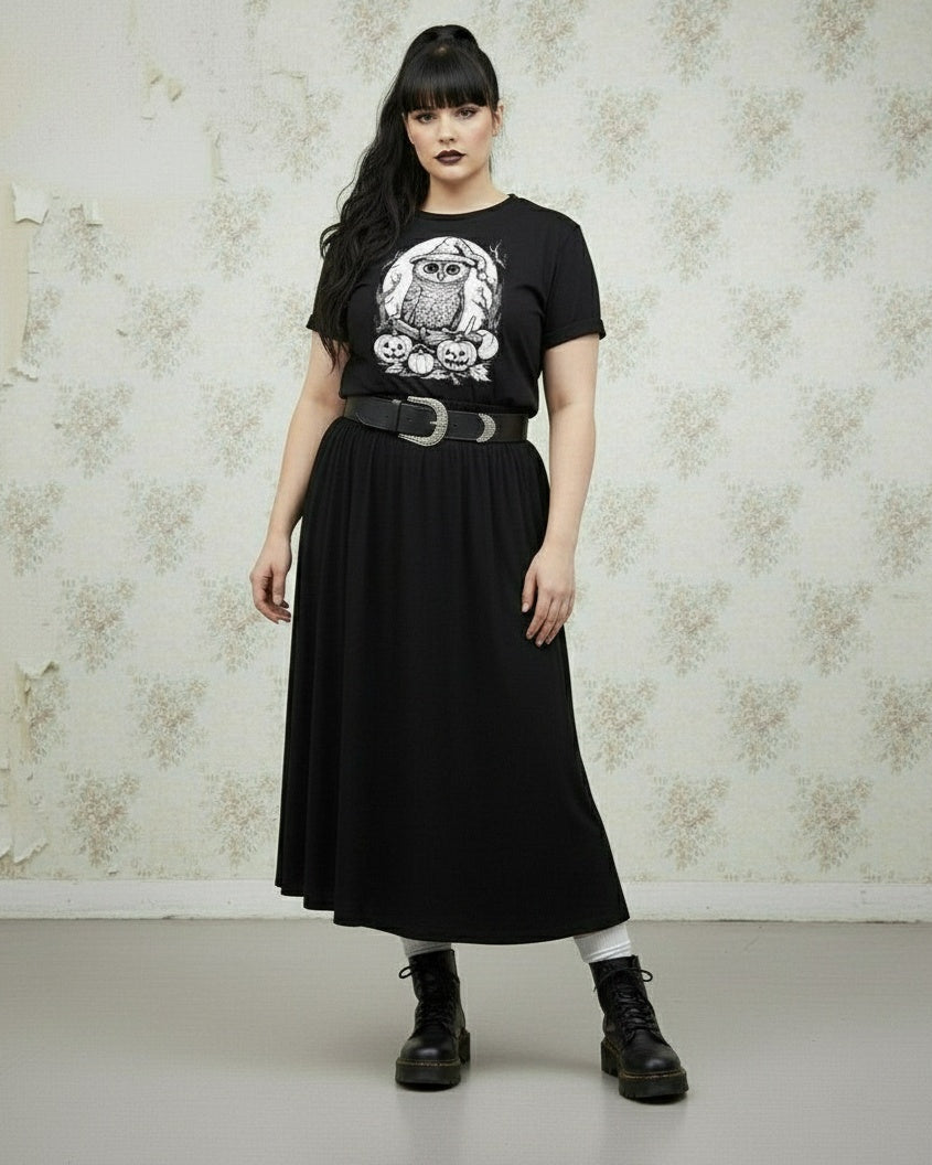 Person wearing a black t-shirt with an owl design and a black skirt against a textured wall.