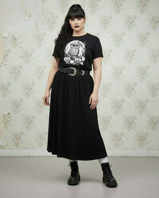 Person wearing a black t-shirt with an owl design and a black skirt against a textured wall.
