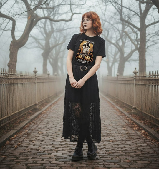 Person wearing a black t-shirt with a graphic design and a long black dress standing on a foggy path.