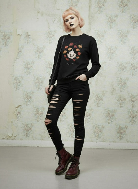 Person wearing a black sweater with a floral design and ripped black jeans against a textured wall.
