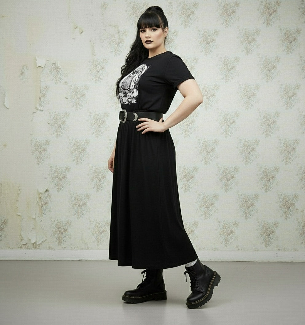 Woman wearing a black t-shirt with a graphic design and a long black skirt against a floral wallpaper background.