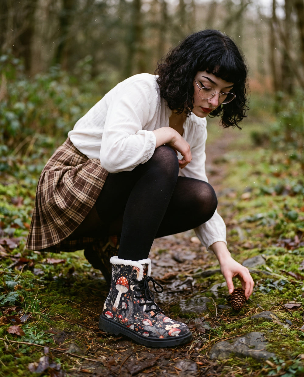 Woman in a white blouse and plaid skirt crouching on a woodland path wearing Amanita Winter Boots