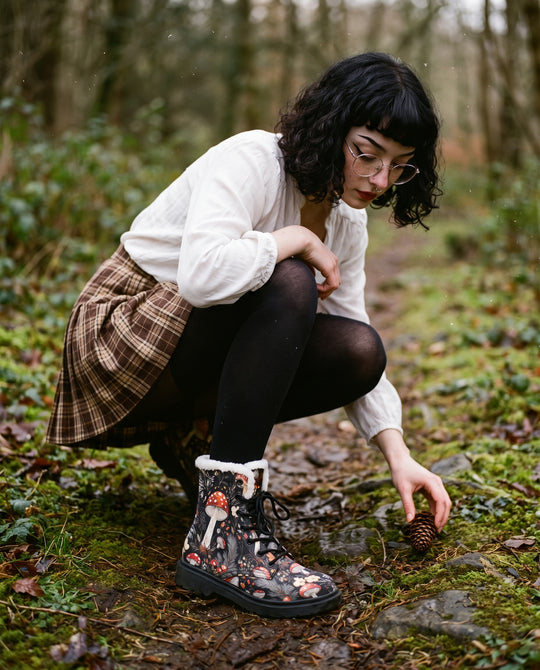 Woman in a white blouse and plaid skirt crouching on a woodland path wearing Amanita Winter Boots