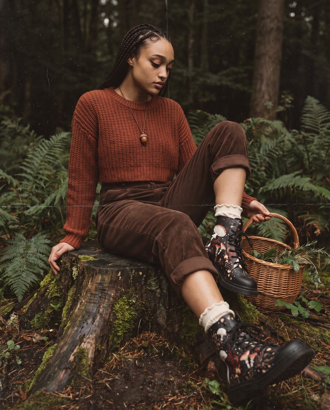 Woman in a rust jumper and brown corduroy trousers sitting on a tree stump in a forest wearing Faery Fungi Boots